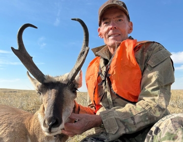 An experienced hunter, clad in an orange safety vest, poses beside their antelope, symbolizing years of passion for hunting and an exciting guided experience with SNS Outfitter & Guides.